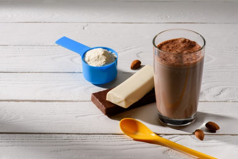 glass of protein shake with energy bars on white wooden table