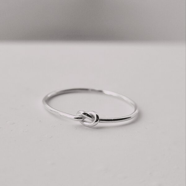 Här är en ring i silver. Det är en rund tråd som är 1 mm tjock. Ovansidan av ringen består av en enkel knut. Knuten är lätt åtdragen. Polerat silver.