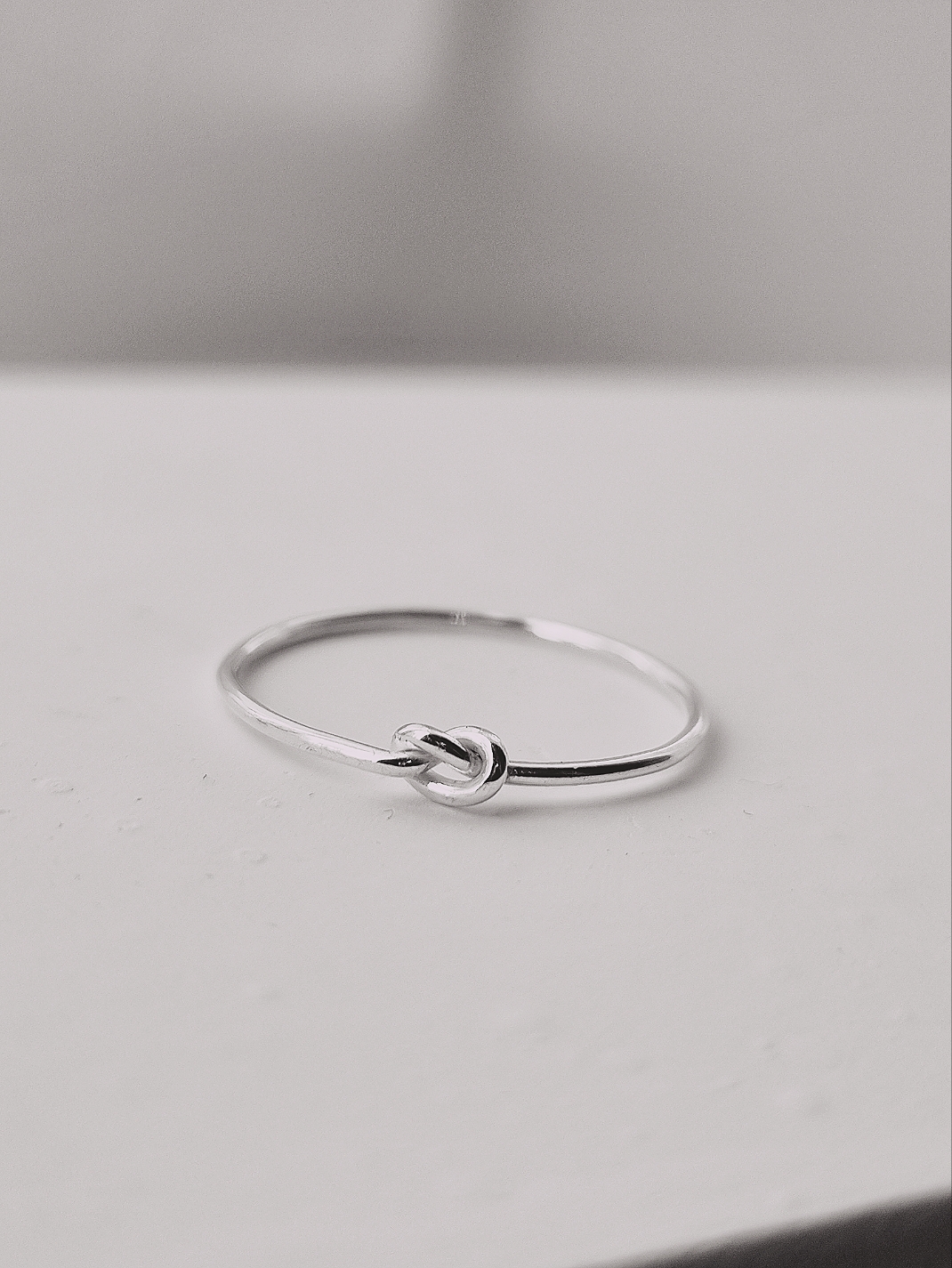 Här är en ring i silver. Det är en rund tråd som är 1 mm tjock. Ovansidan av ringen består av en enkel knut. Knuten är lätt åtdragen. Polerat silver.
