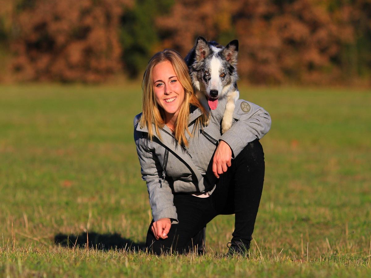 Dog Dancing. Blonde Frau kniet auf dem Boden und hat Ihren Hund auf der Schulter.