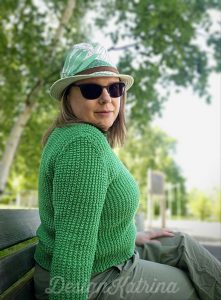 Copyright: DesignKatrina.se
Nightingale pullover, version testknitted by DesignKatrina. 
*Woman sitting on a bench in a green sweater, pants and hat + brown sunglasses.*