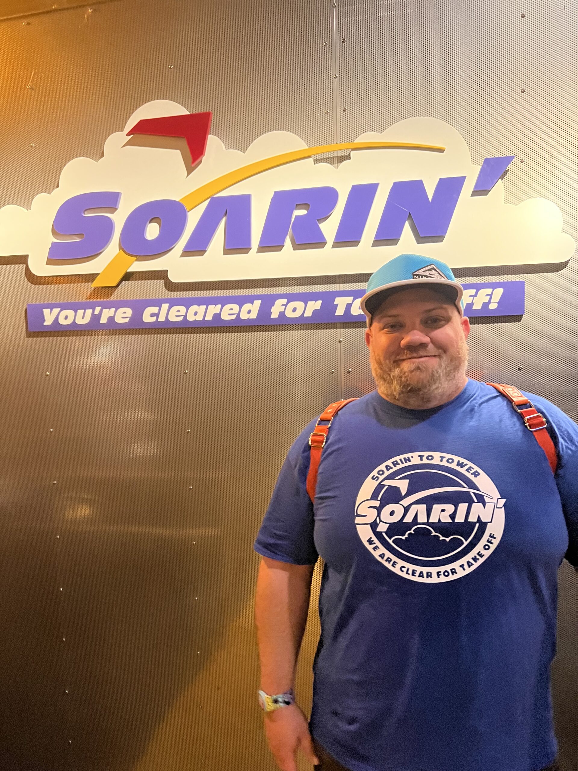 Beans is stood under the Soarin' sign in the queue, wearing a Soarin' T-Shirt