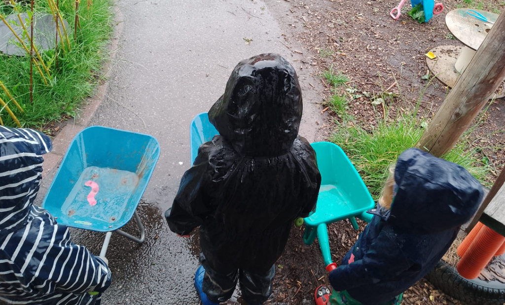 Children standing in the rain in puddle suits