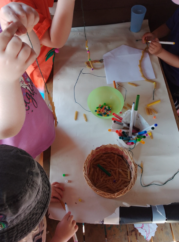Children around a table making necklaces out of pasta and beads