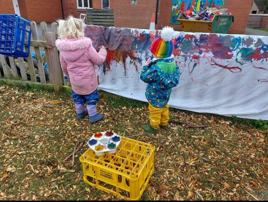 Children painting a large sheet on a fence at Dodleston Pre-School