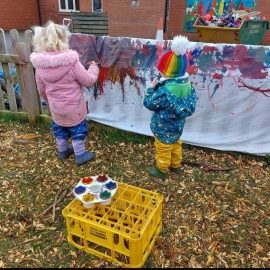 Children painting a large sheet on a fence at Dodleston Pre-School