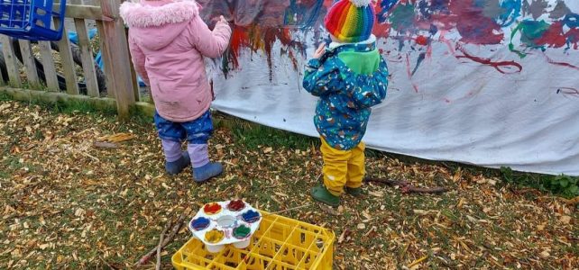 Children painting a large sheet on a fence at Dodleston Pre-School