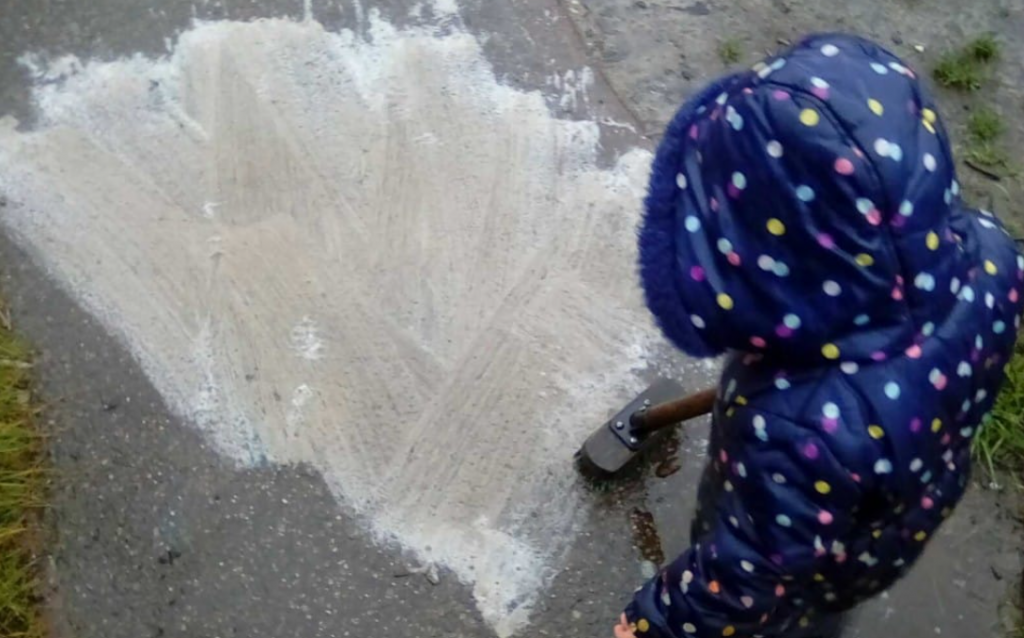 A child using a brush to foam washing-up liquid into concrete