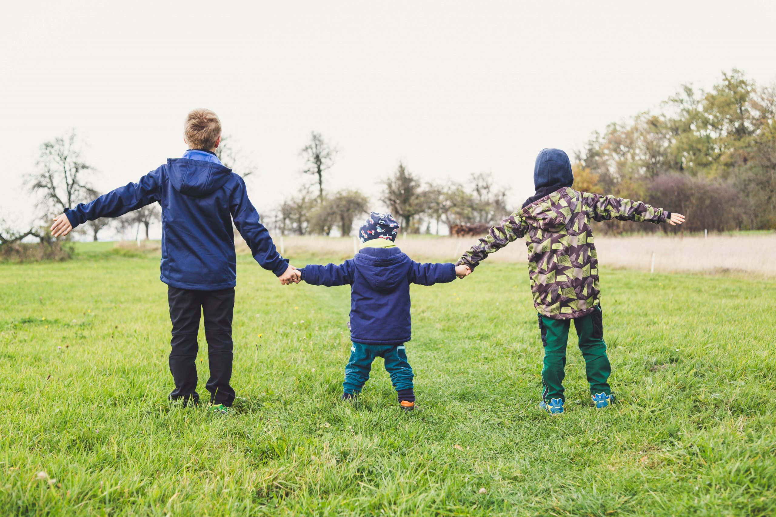 Three children of different ages holding hands outside in a field