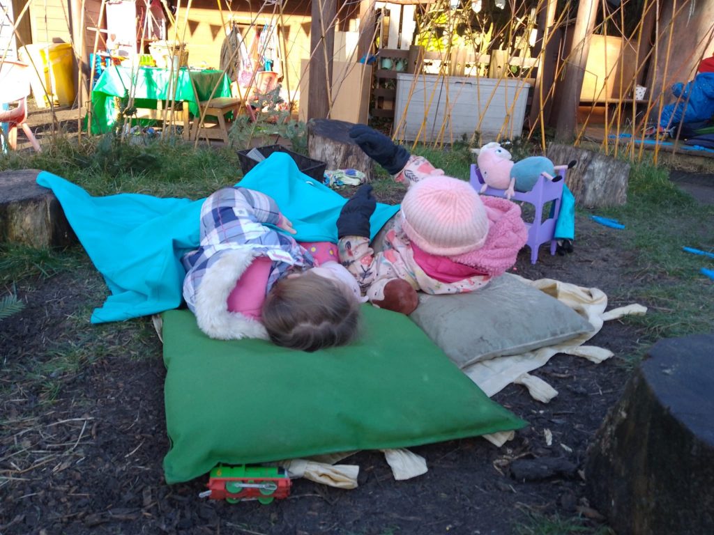 Two children lying in beds on the ground to go 'camping'