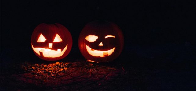 Two pumpkins with faces carved into them lit up by candles