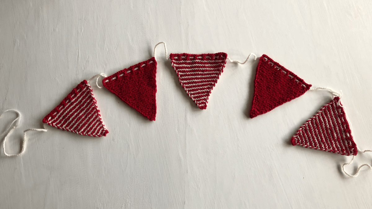 A picture of a knitted red and white Christmas bunting laying on a white table