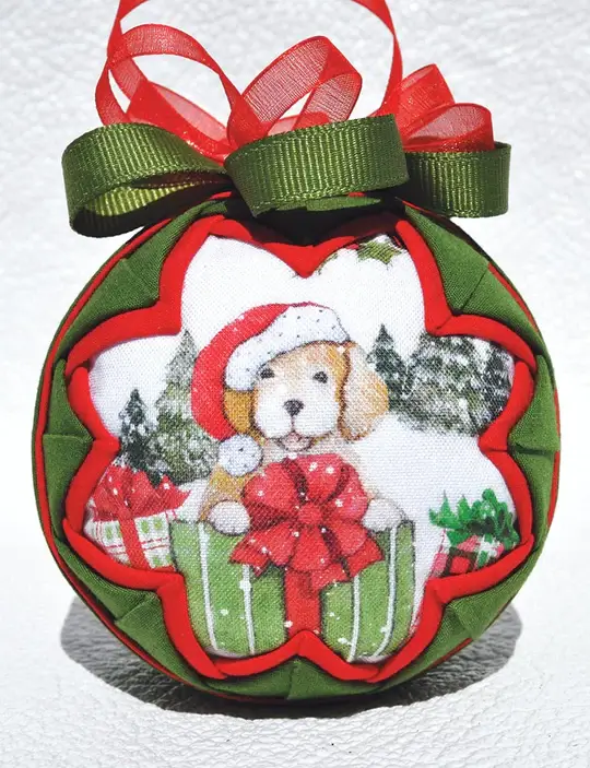 image showing a quilt christmas ornament kit. with a cute puppy wearing a santa hat framed with red and green fabric folds.