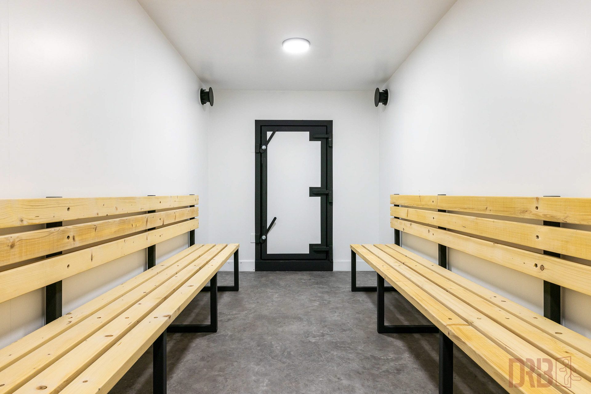 Seating Area in the Container Bunker A seating area in a container bunker with sturdy wooden benches on both sides and a robust door at the end of the room.