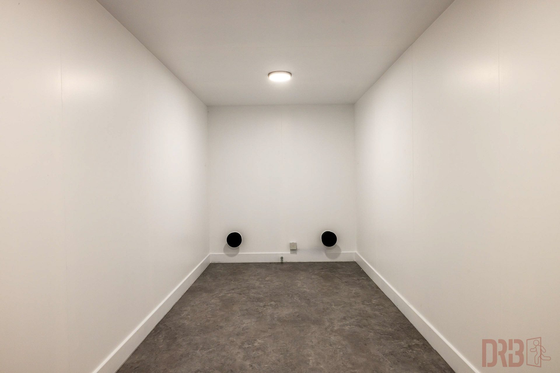 Empty Room in the Bunker An empty room in a bunker with white walls, a concrete floor, and two round ventilation openings for good air circulation.