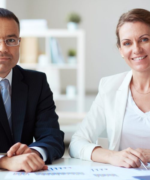 Two mature business partners looking at camera in office