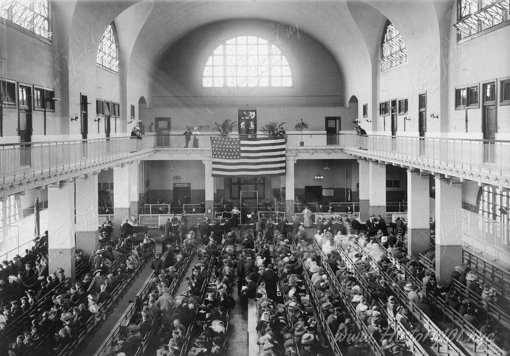 watermark_1024_1.1902-RETOUCHED-Ellis-Island—Immigrants-Seated-on-Long-Benches-in-Main-Hall-2661×1858