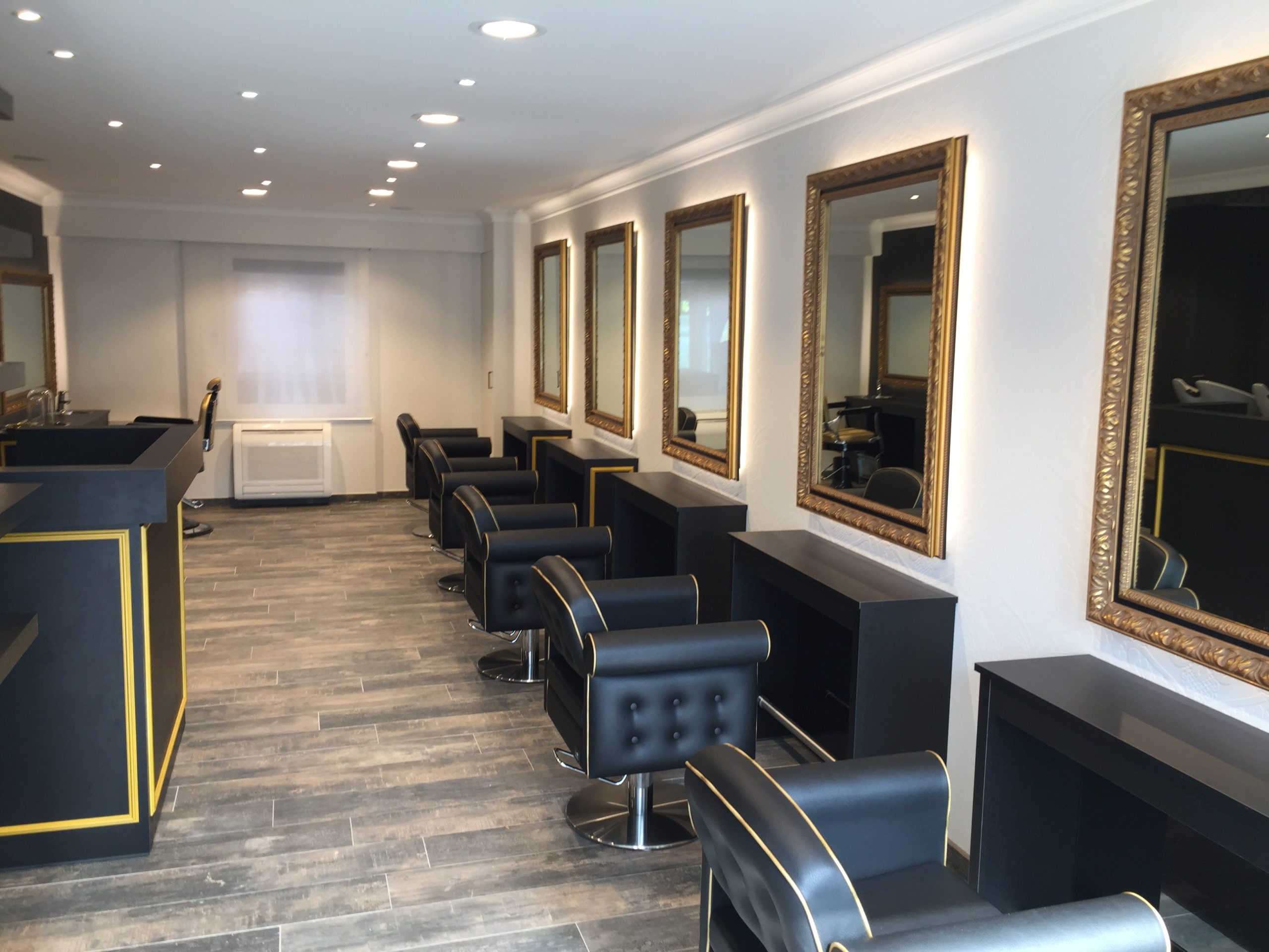 Modern en luxueus interieur van kapsalon met zwarte stoelen, grote spiegels en warme verlichting.