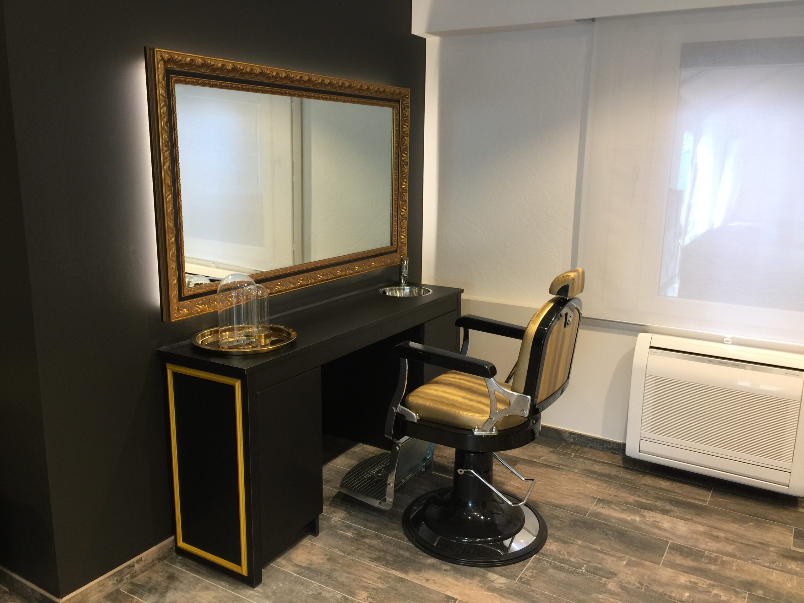 Stijlvolle kappersstoel met spiegel en zwart meubel met gouden accenten in een modern saloninterieur.