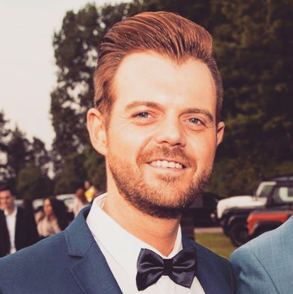Man met kort, naar achter gestyled haar en verzorgde baard, gekleed in een pak met vlinderdas voor een stijlvolle en formele uitstraling.