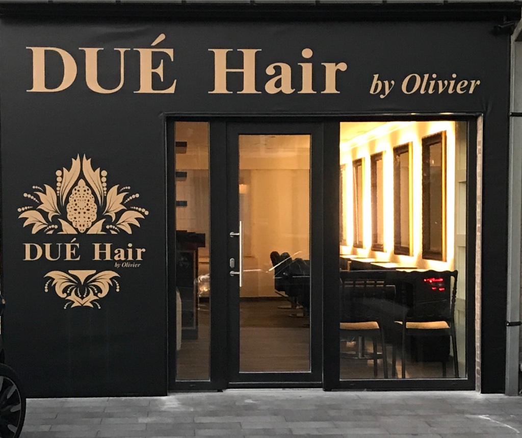 Vooraanzicht van kapsalon Dué Hair by Olivier met zwarte gevel, gouden logo en stijlvolle ingang.