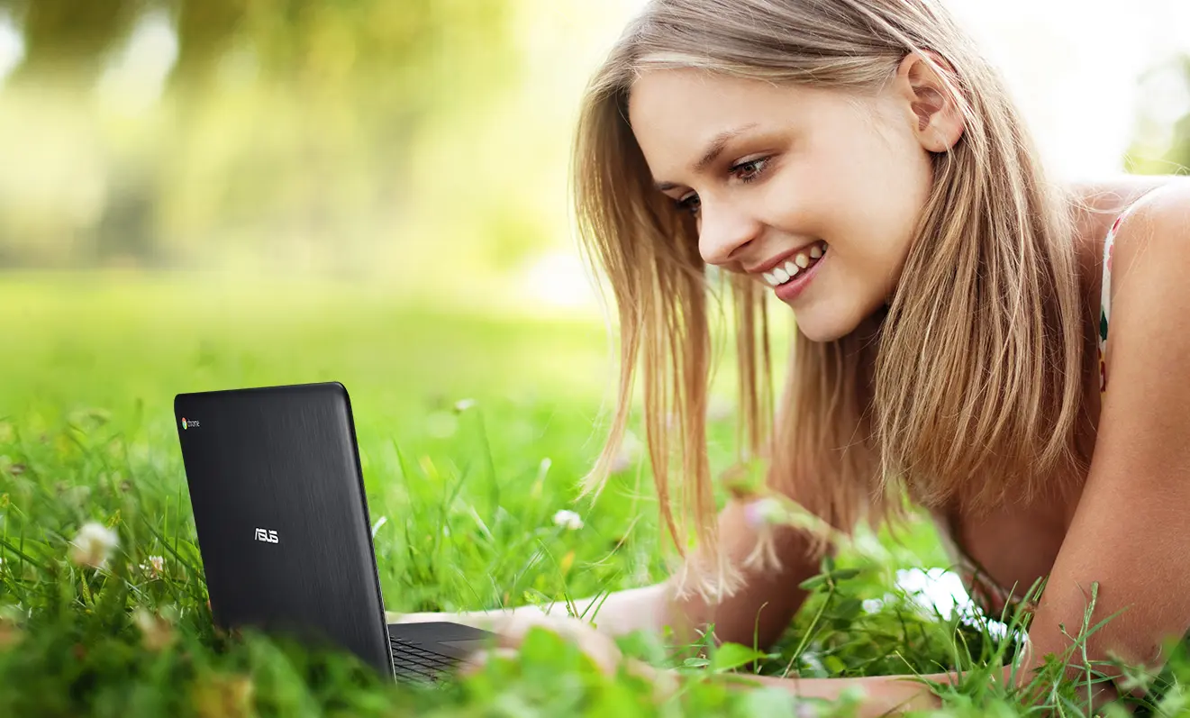 Ung pige i sommerkjole bruger en ASUS Chromebook i en park.