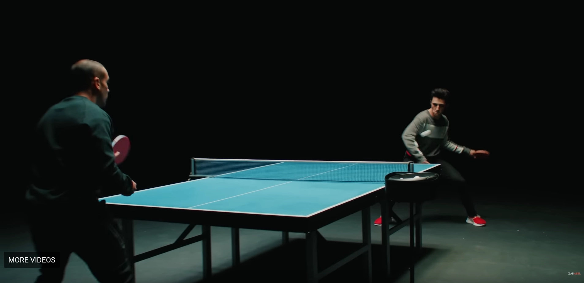 A dynamic scene where Zak Abel receives table tennis coaching from Eli Baraty during the music video for "Everybody Needs Love." Both individuals are focused and engaged, with Abel preparing for a shot under Baraty's attentive guidance, showcasing a moment of learning and determination amidst the rhythm of the song.