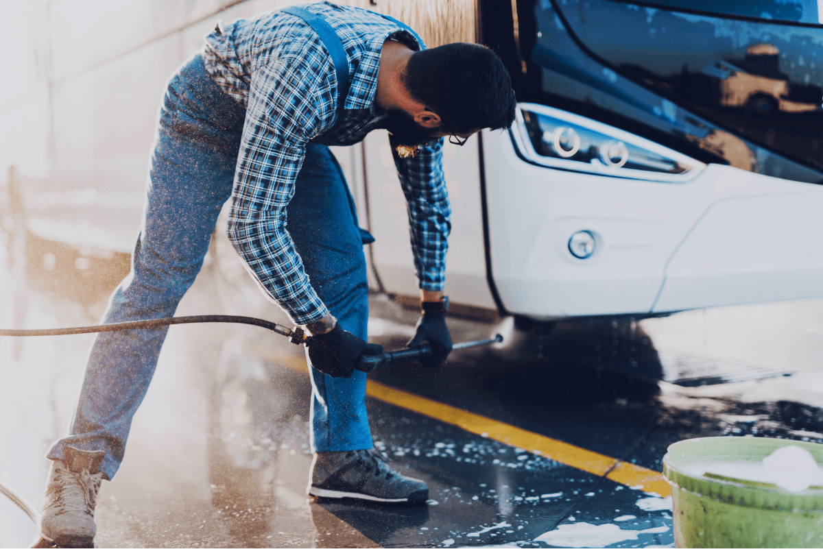 Young man washing bus using high pressure water selective focus