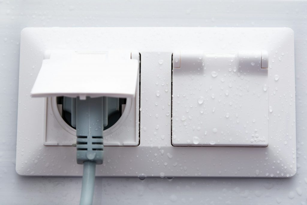 Weatherproof socket on a white tiled wall with water droplets.