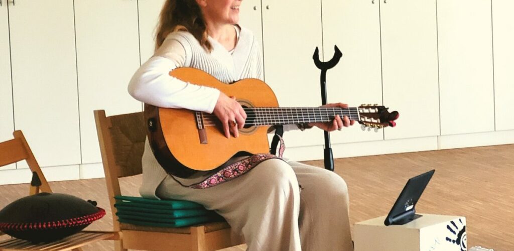 Elena Deppe als Singleiterin mit Gitarre auf einem Stuhl sitzend.