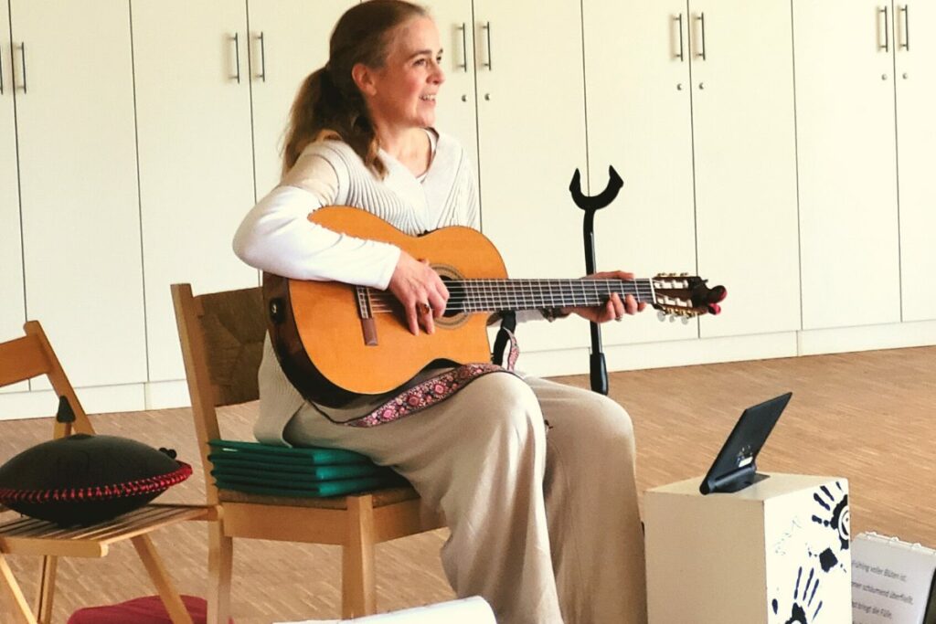 Elena Deppe als Singleiterin mit Gitarre auf einem Stuhl sitzend.