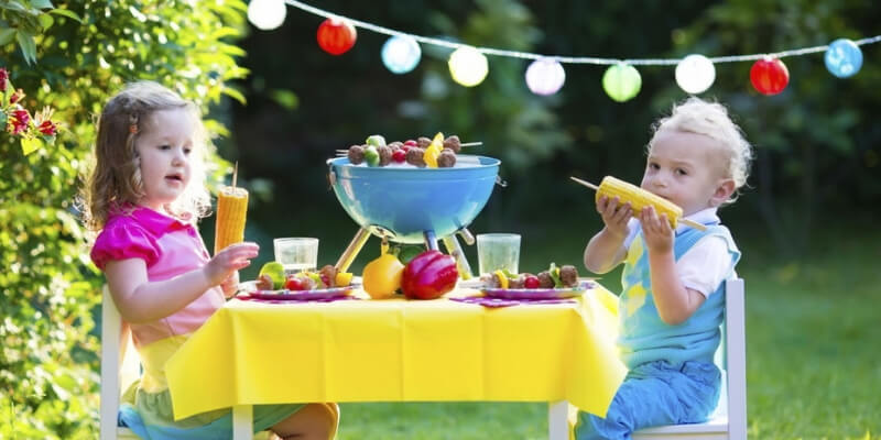 due bambini mangiano pannocchie su un tavolino allestito all'aperto