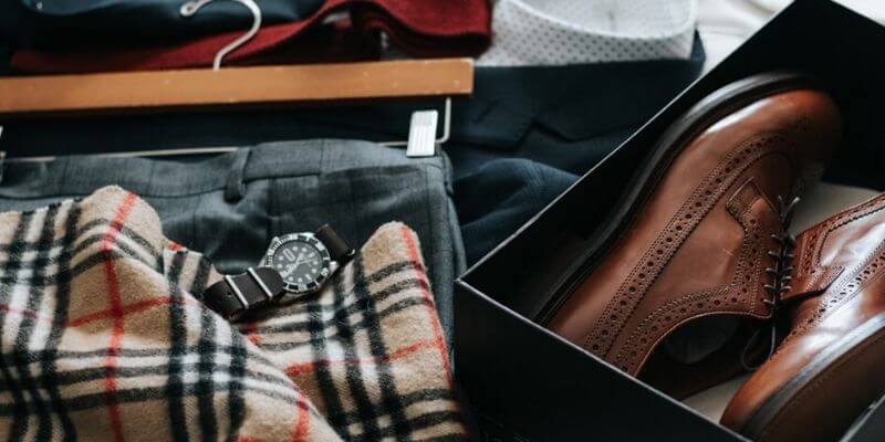 una sciarpa, un orologio e un completo e delle scarpe su un letto, come se si dovesse preparare una valigia