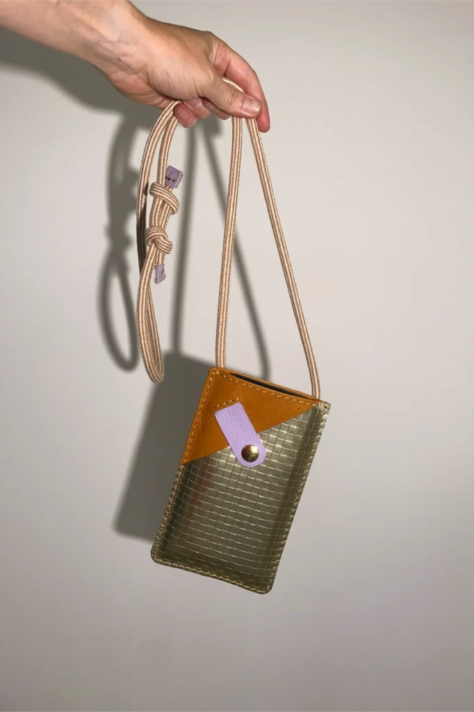 Cognac leren smartphonetasje uit The Cord Series van Elise Verdegem. Afgewerkt met een goudkleurig zakje voor (bank)kaarten.