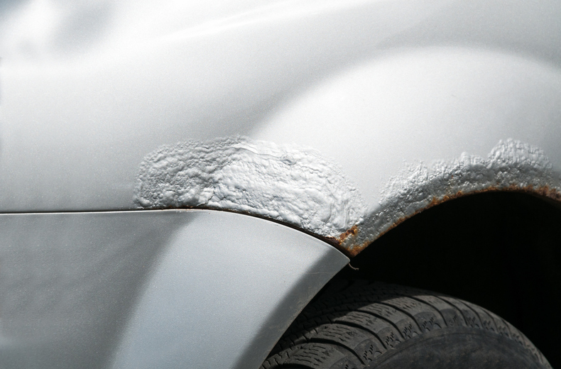 Silver car broken side with damaged metal with rusty paint and corrosion above the tire