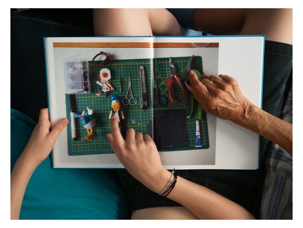 lawrence and his grandmother are looking in the book 'sometimes i am fourteen'young and old hands are pointing at photographs in the book