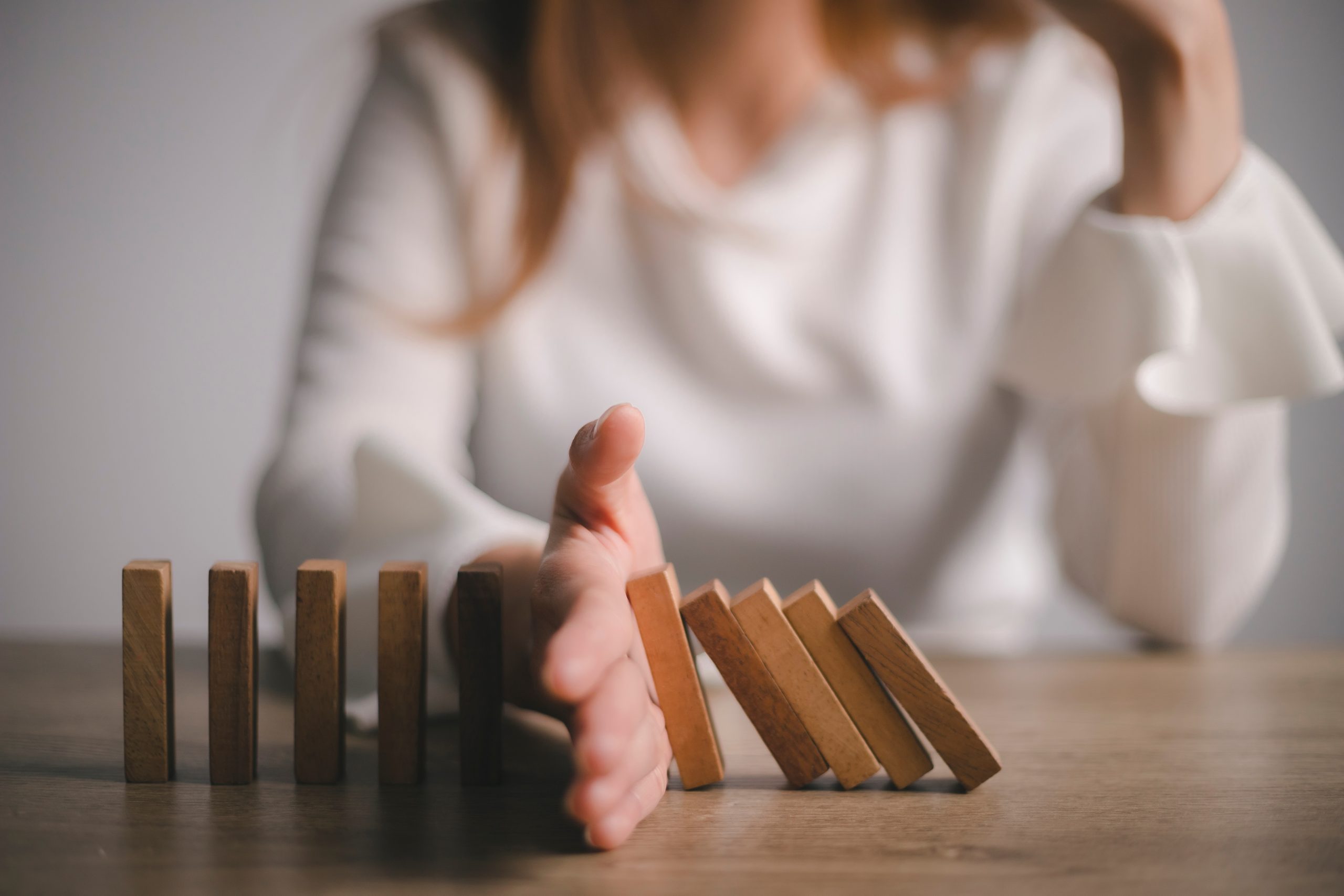 Een persoon legt haar hand tussen domino blokjes. En geeft aan, tot hier en niet verder.