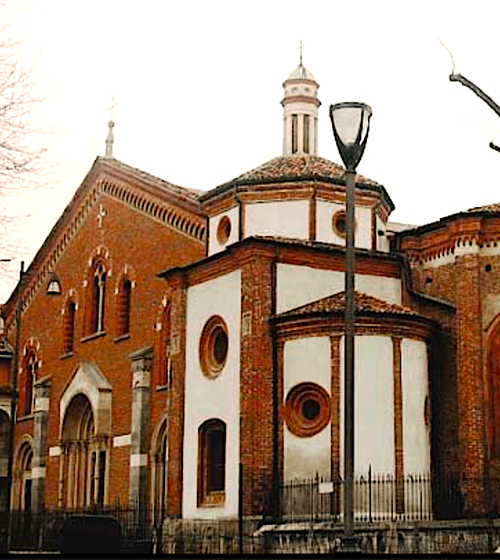 Grande chiesa di mattoni rossi e bianchi con finestre rotonde. L'entrata è fatta di marmo grigio chiaro. Intorno alla chiesa c'è un muretto dicemento e sopra di esso una recinzione metallica.