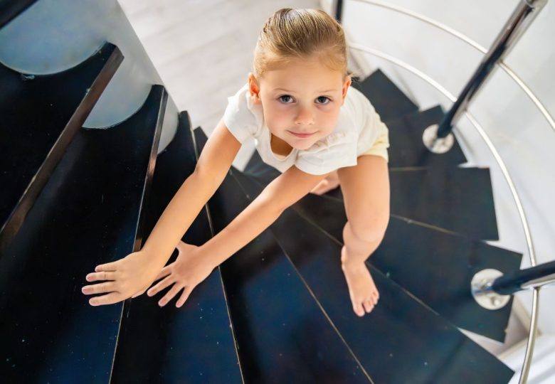 Niña rubia subiendo por una escalera de caracol negra