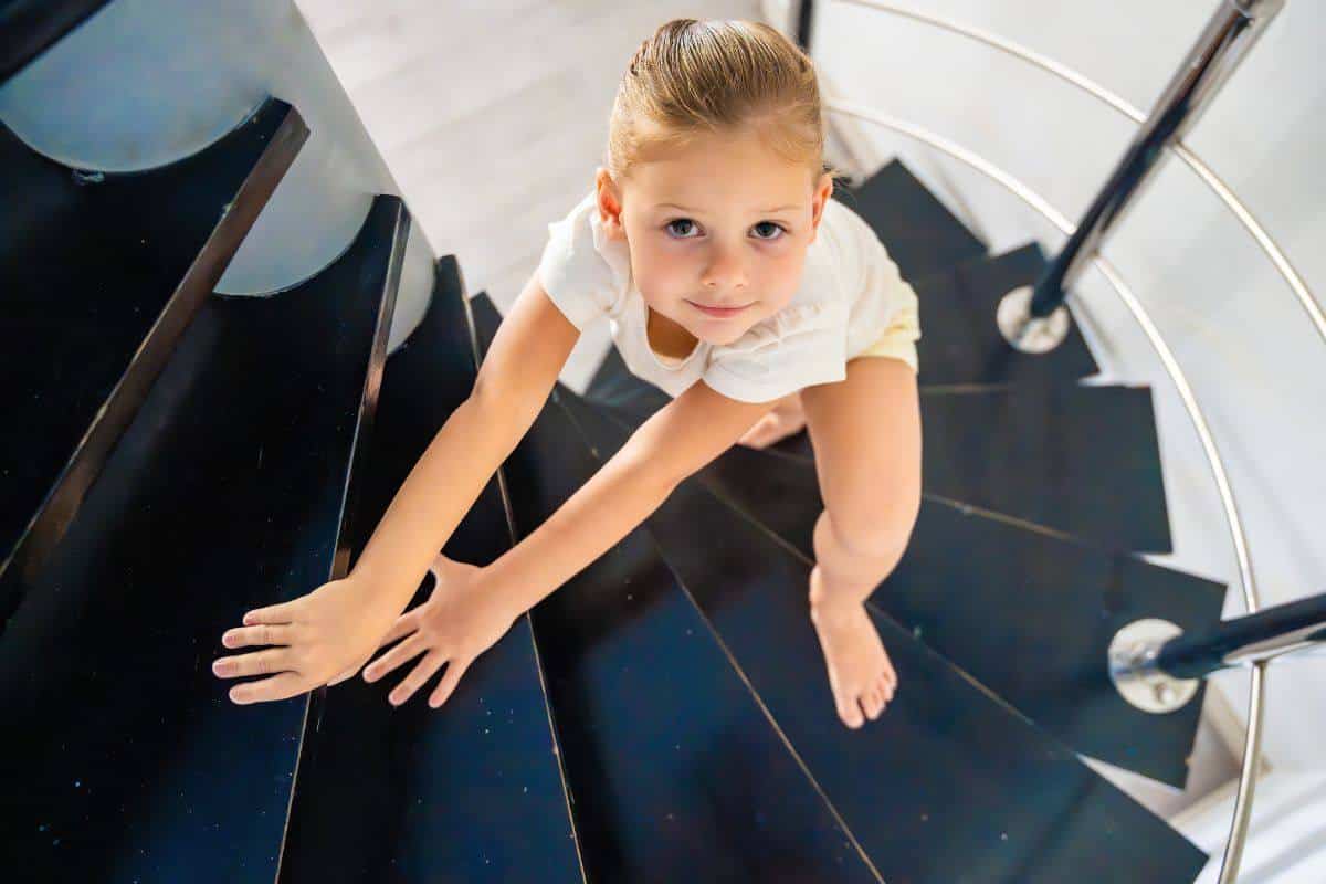 Niña rubia subiendo por una escalera de caracol negra