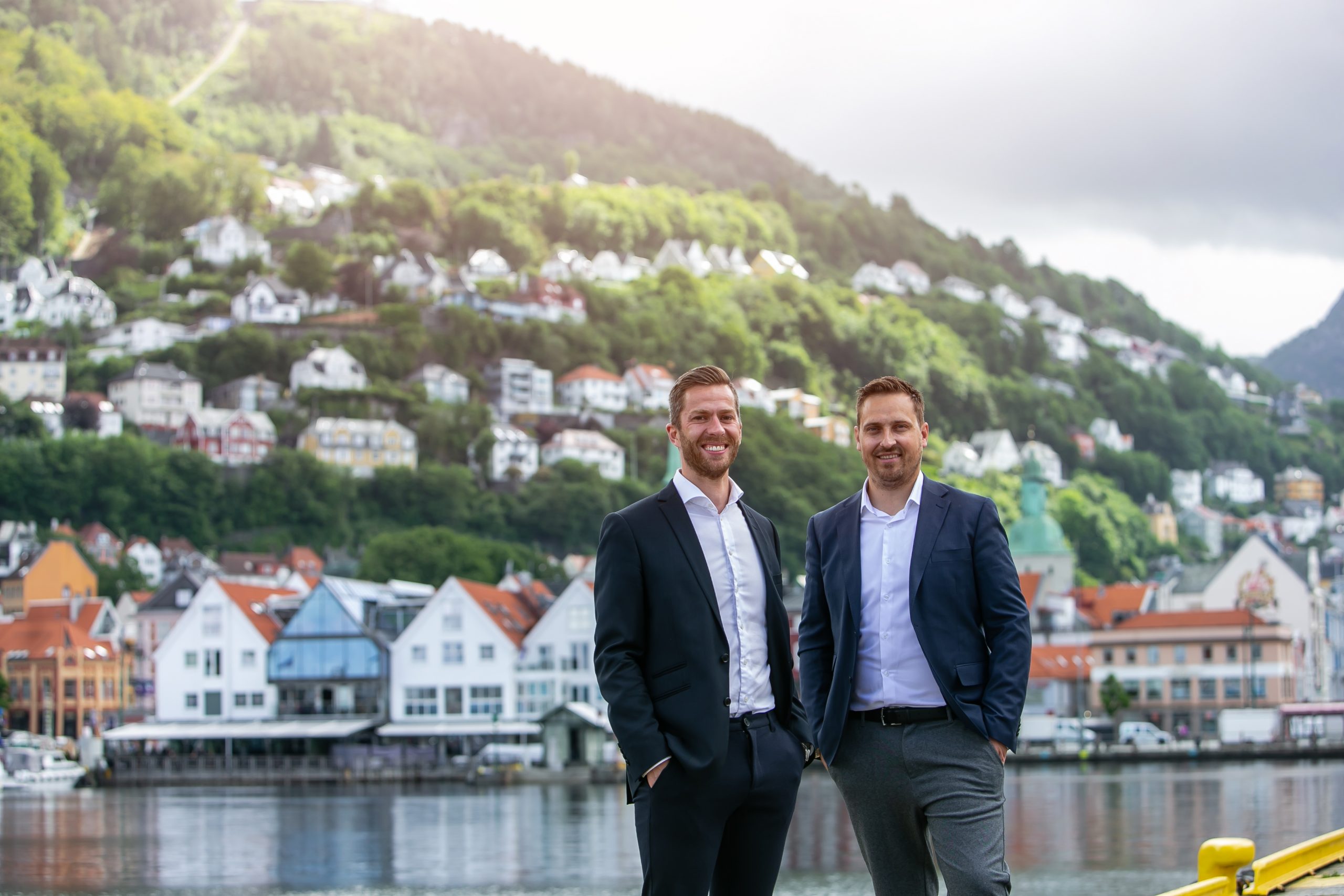 To personer står på Strandkaien med utsikt mot Zachariasbryggen, Fløyen og Skansemyren i Bergen.