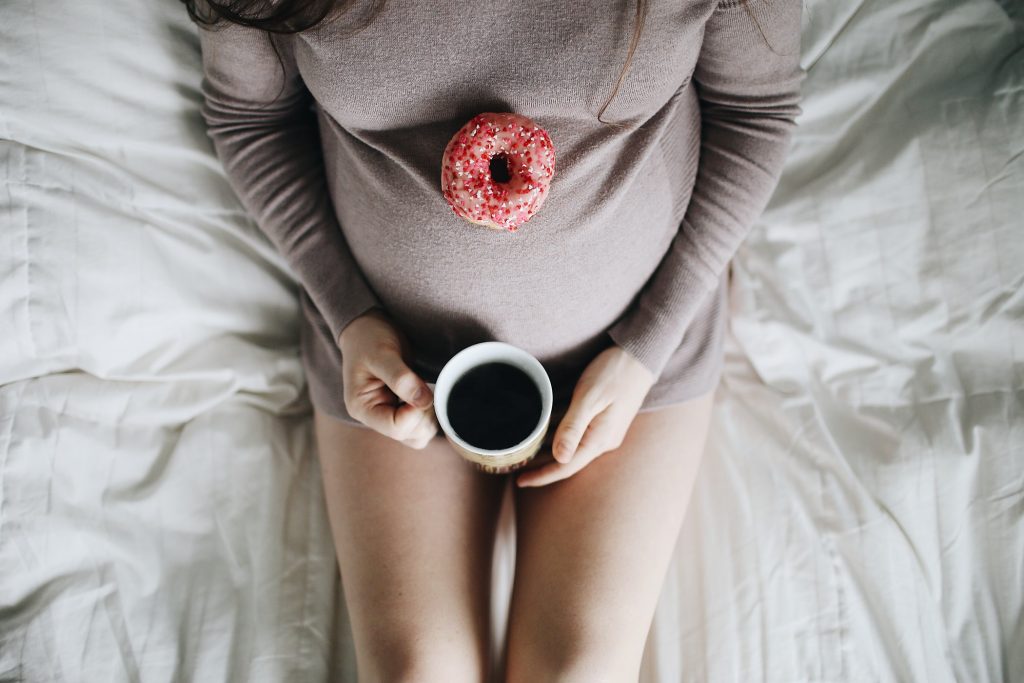 virtuele babyshower: zwangere vrouw met koffietas in de handen en roze donut op de buik