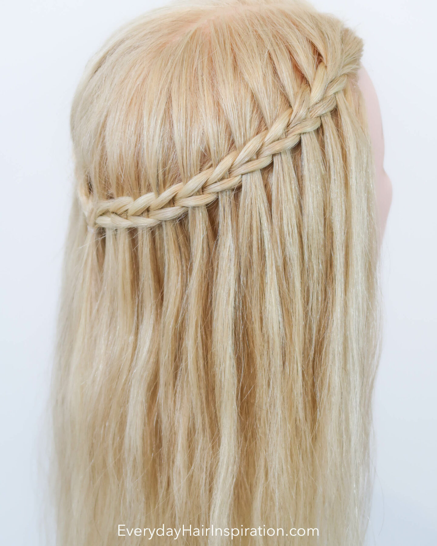 Blonde hairdresser head with a half up half down hair styles with a scissor waterfall braid, seen from the back at an angle.