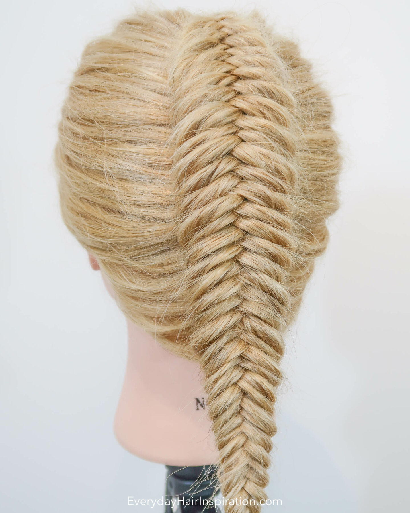 Blonde hairdresser doll seen from the back at an angle, with a single dutch fishtail braid in the hair