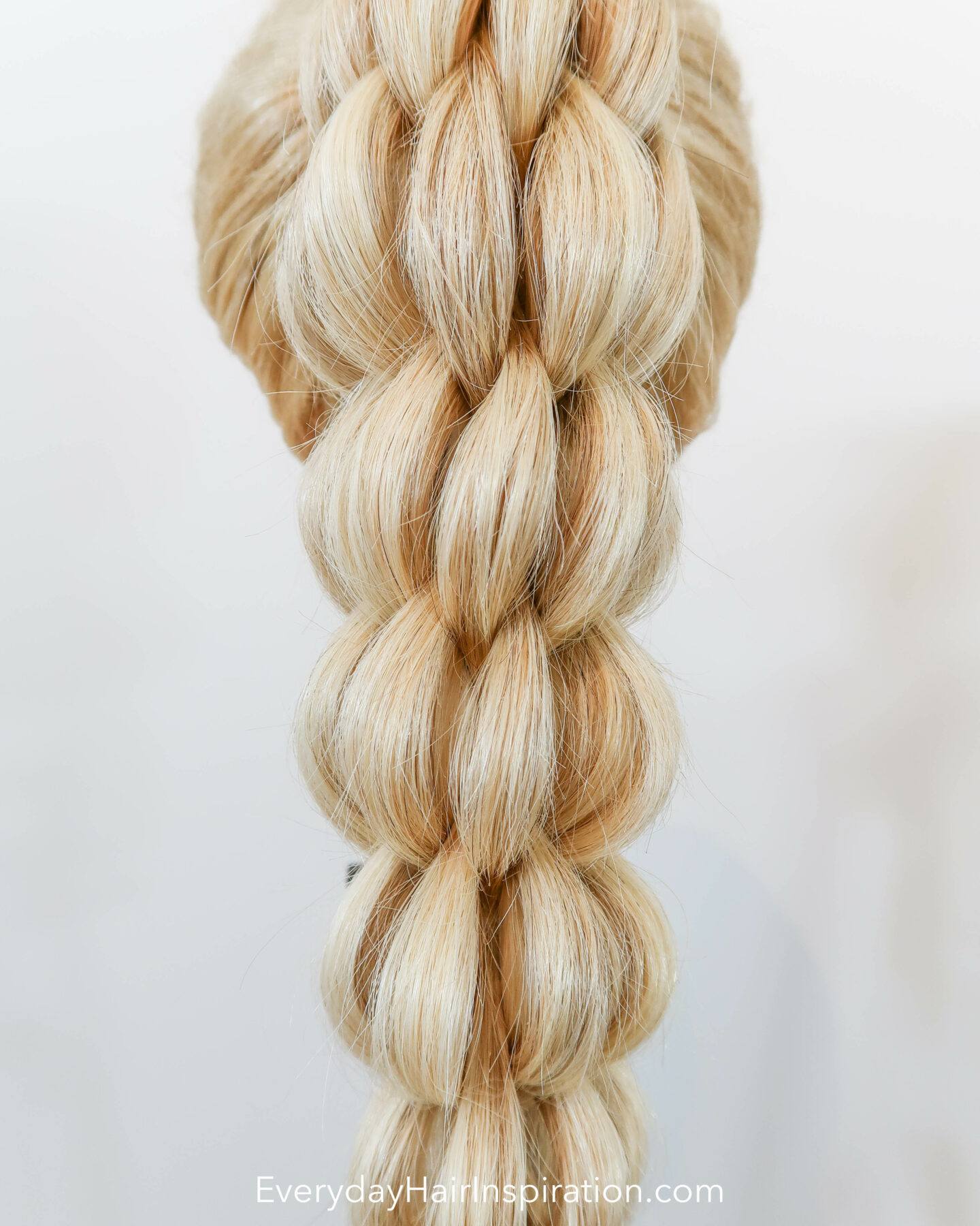 Blonde hairdresser doll seen from the back with a high ponytail in the hair. The ponytail is braided into a 3d pull through braid. Closeup of the hair.