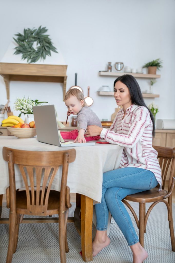 Young mom working at laptop, daughter interfering