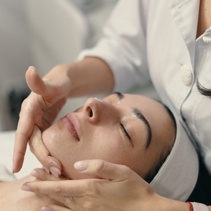 Beauty, spa and cosmetology concept. Young woman lies with closed eyes, cosmetologist making procedure for facial skin rejuvenation, facial massage.