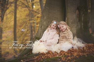 To søstre sidder ved foden af et træ i efterårsskoven