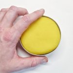 Hånd holder økologisk gul modellervoks pakket i aluminiumsdåse.