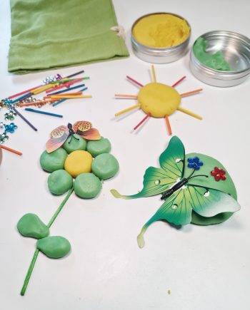 Grøn aktivitetspose til børn indeholder sjov leg med modellervoks i gul og grøn, samt blomster, pinde og sommerfugle.